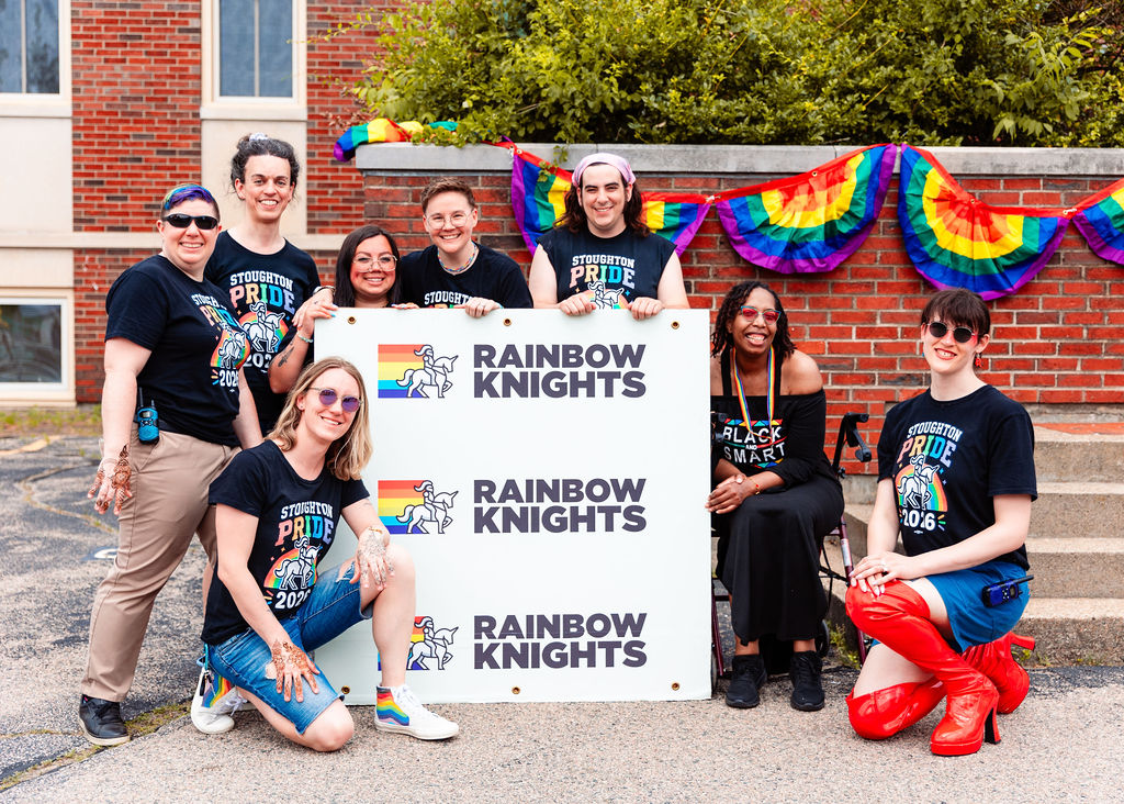 Members of the Rainbow Knights board smiling together with a Rainbow Knights banner at Stoughton Pride